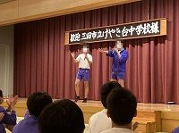 舞台上で青いジャージ姿の生徒さん2人が片手を上げて喋っている様子の写真