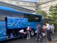 青い観光バスの荷物室に生徒たちの荷物を搭載している様子の写真