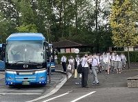 青い観光バスの横で生徒たちが待機する様子の写真