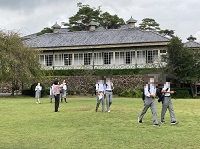 灰色の屋根の建物の前の芝の広場を歩く生徒たちの写真