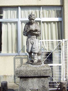 校舎の窓の近くに設置された、薪を背負って読書をしながら歩く姿の二宮金次郎の石像写真