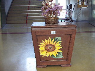 階段前に置かれている、校花であるひまわりが描かれた台と飾られている花の写真